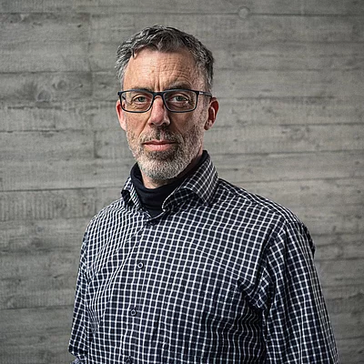 Portrait von Uwe Raabe, Geschäftsführer Technik, vor einer grauen Sichtbetonwand