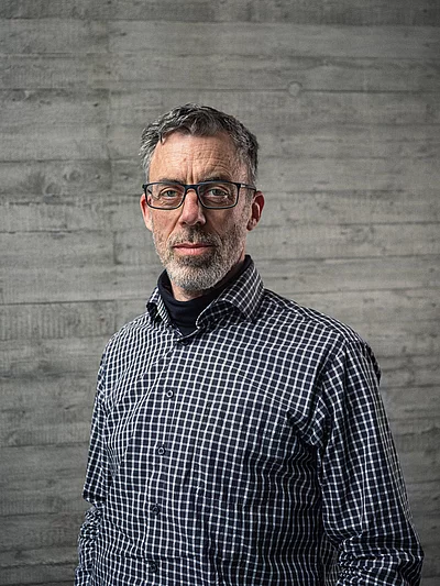 Portrait von Uwe Raabe, Geschäftsführer Technik, vor einer grauen Sichtbetonwand