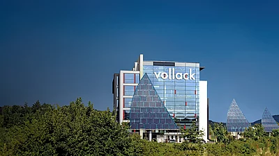 Panorama-Ansicht des Vollack-Firmengebäudes mit einem Photovoltaik-Segel vor blauem Himmel.