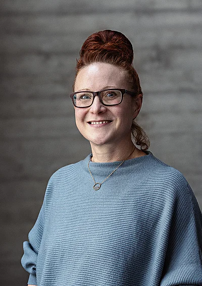 Portrait von Katharina, Teamlead Projektmanagement vor einer grauen Sichtbetonwand