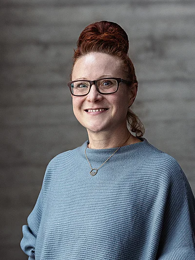 Portrait von Katharina, Teamlead Projektmanagement vor einer grauen Sichtbetonwand